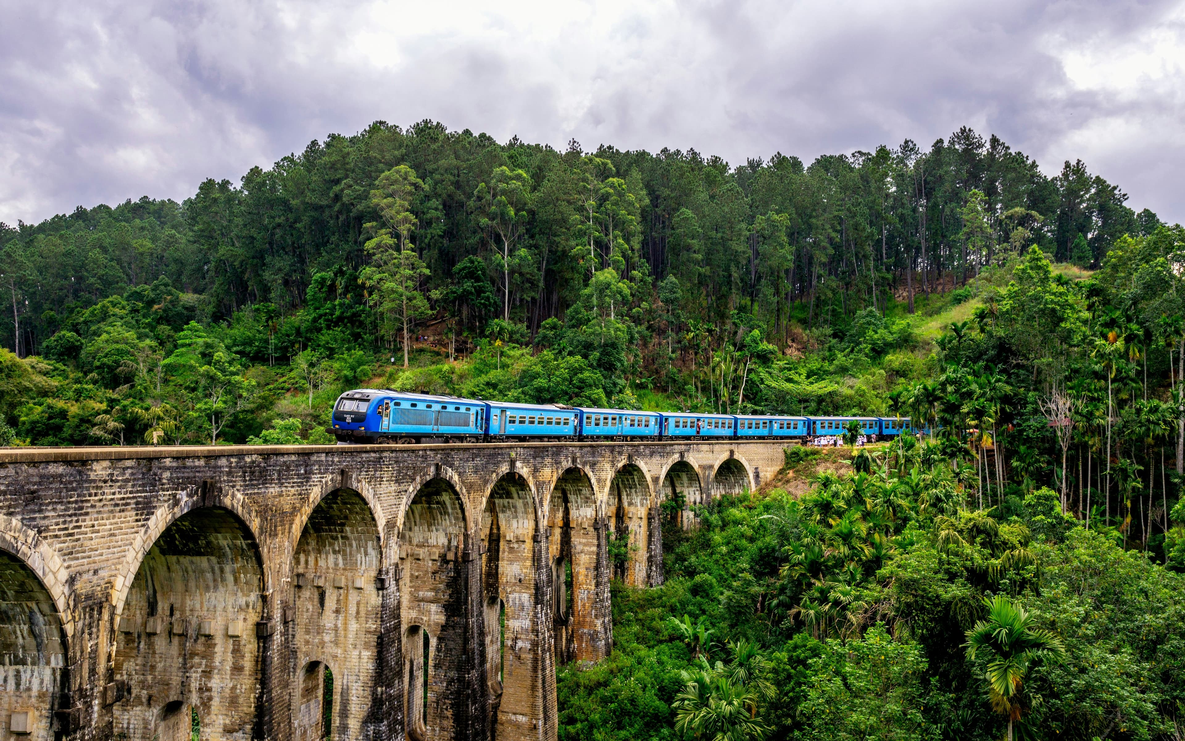 A blue train crossing the Nine Arches Bridge through the forest near Ella